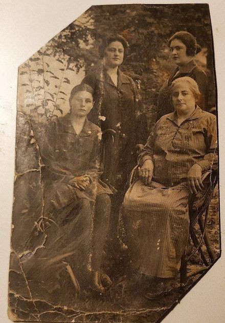 Four women posing outdoors, sepia-toned. One seated, others standing. Possibly a family portrait.