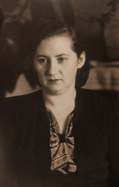 Woman in dark blazer, gazing forward. Her necktie has a patterned design. Sepia-toned photograph.