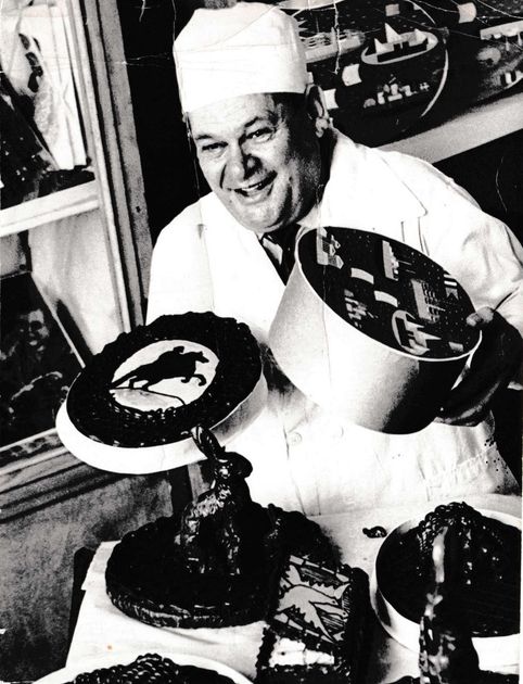Baker holding cakes with decorative tops, smiling in a shop.