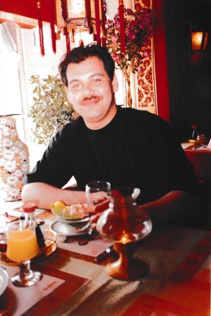 Man seated at a table in a restaurant smiling; orange juice and food on the table.