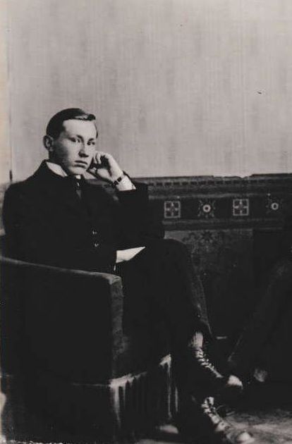 Man in suit seated in armchair, hand to face, gazing off camera. Black and white photo.