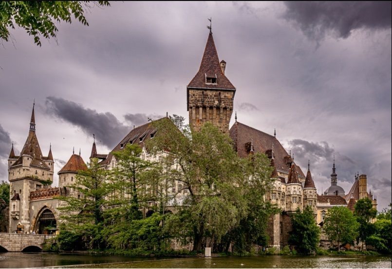 Fairytale castle with multiple towers on a lake, under a cloudy sky.