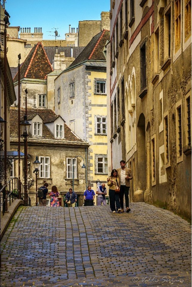 Cobblestone street lined with buildings, people walking. Some with a yellow and red roof.