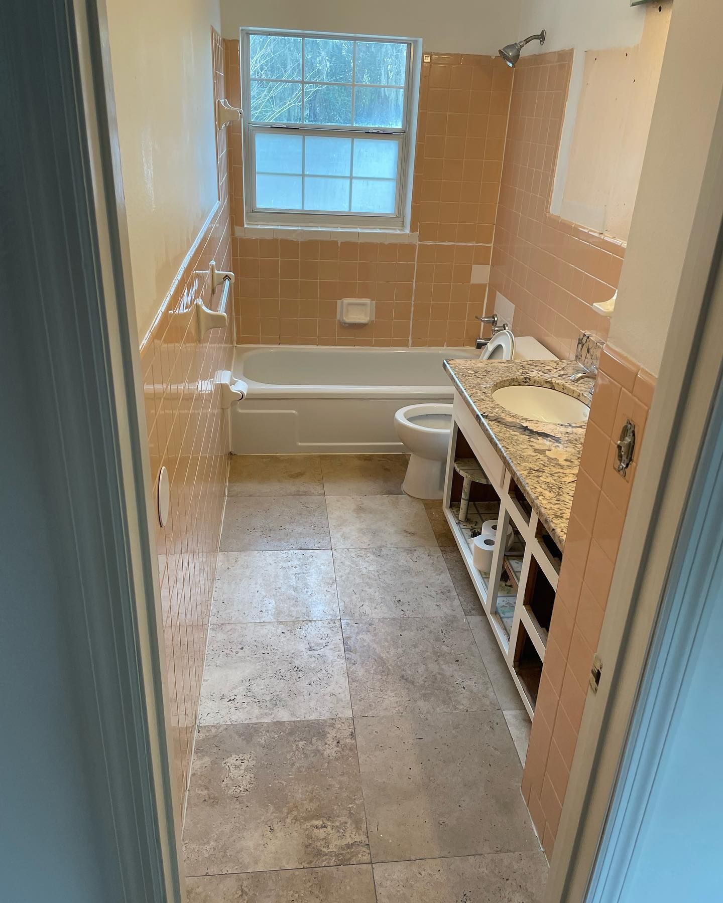 Bathroom with peach tiles, white tub, window, and vanity under renovation.