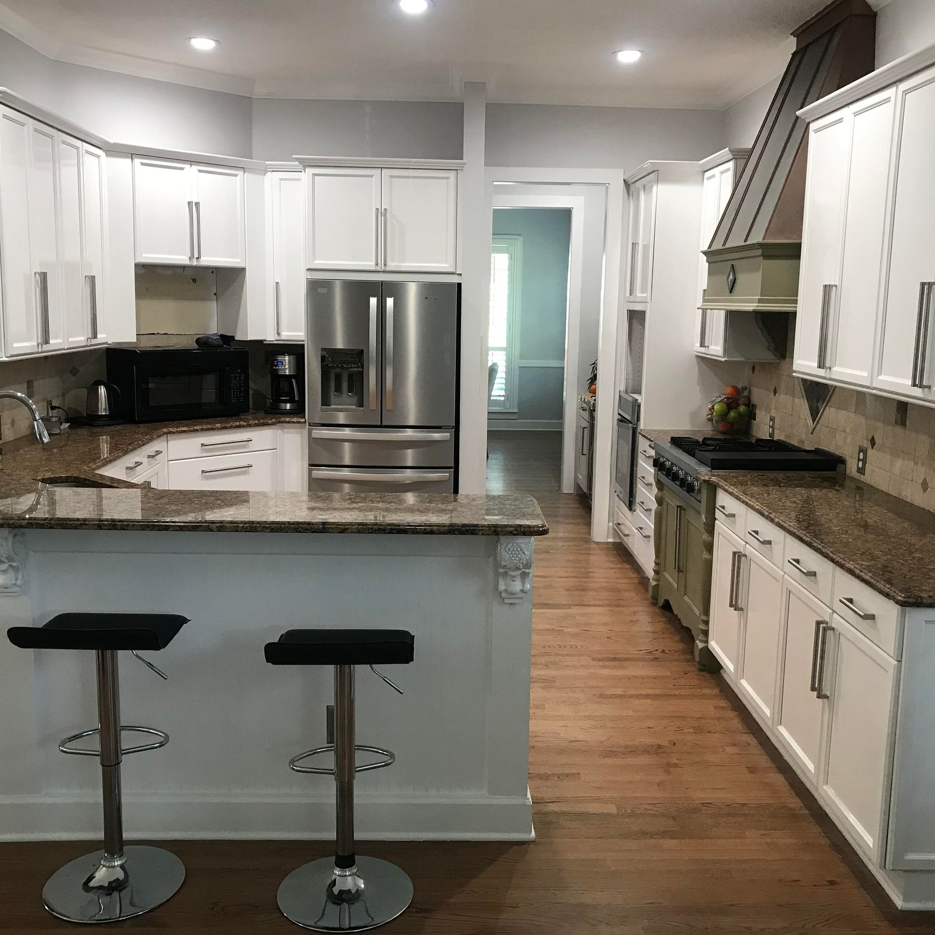 White kitchen with granite countertops, stainless steel appliances, and two bar stools.
