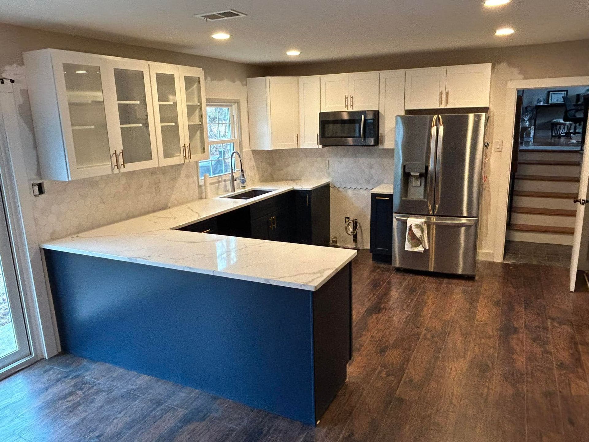 Modern kitchen with white and navy cabinets, stainless steel appliances, and white countertops.