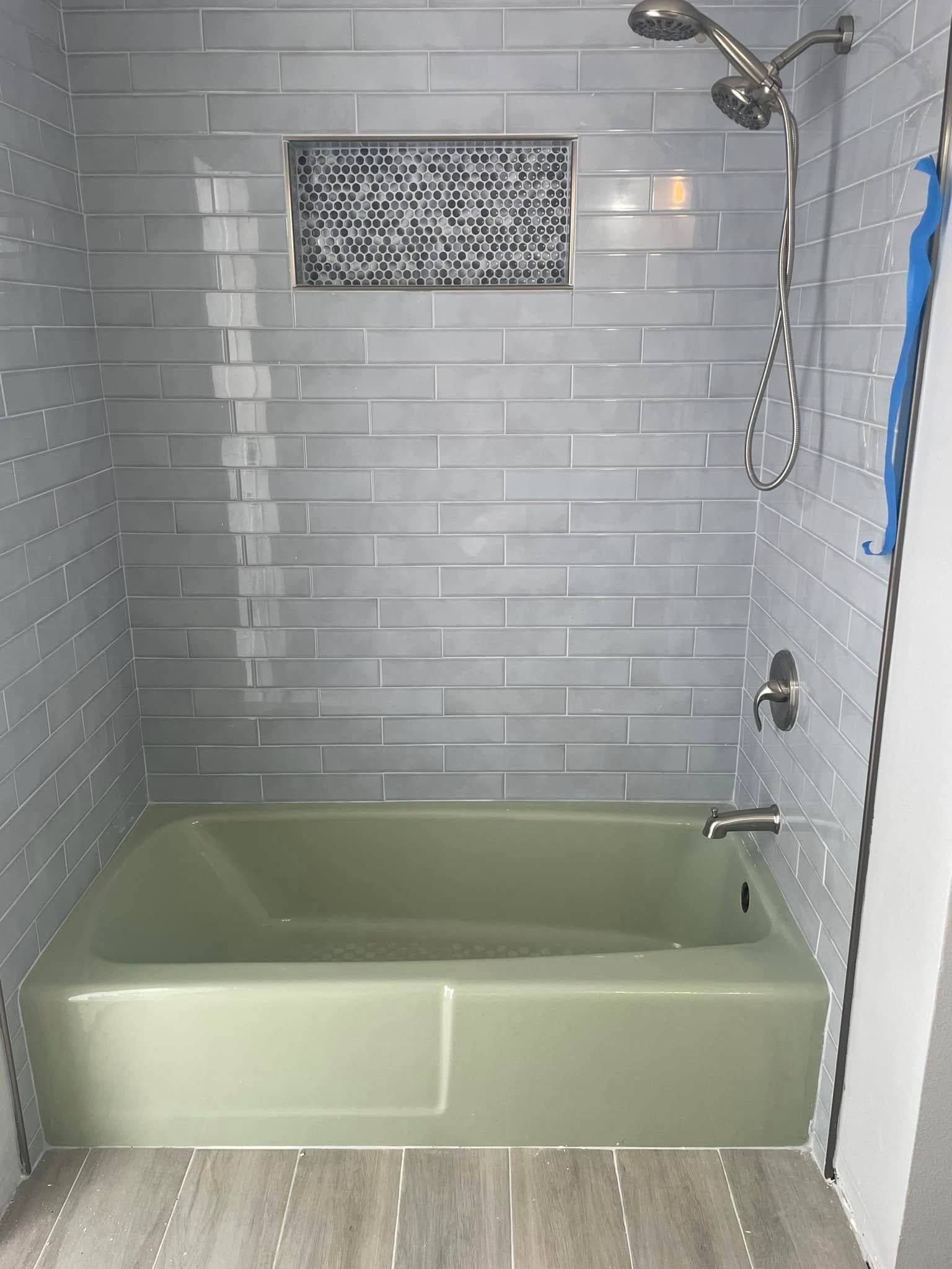 Light green bathtub with gray tiled walls and showerhead.