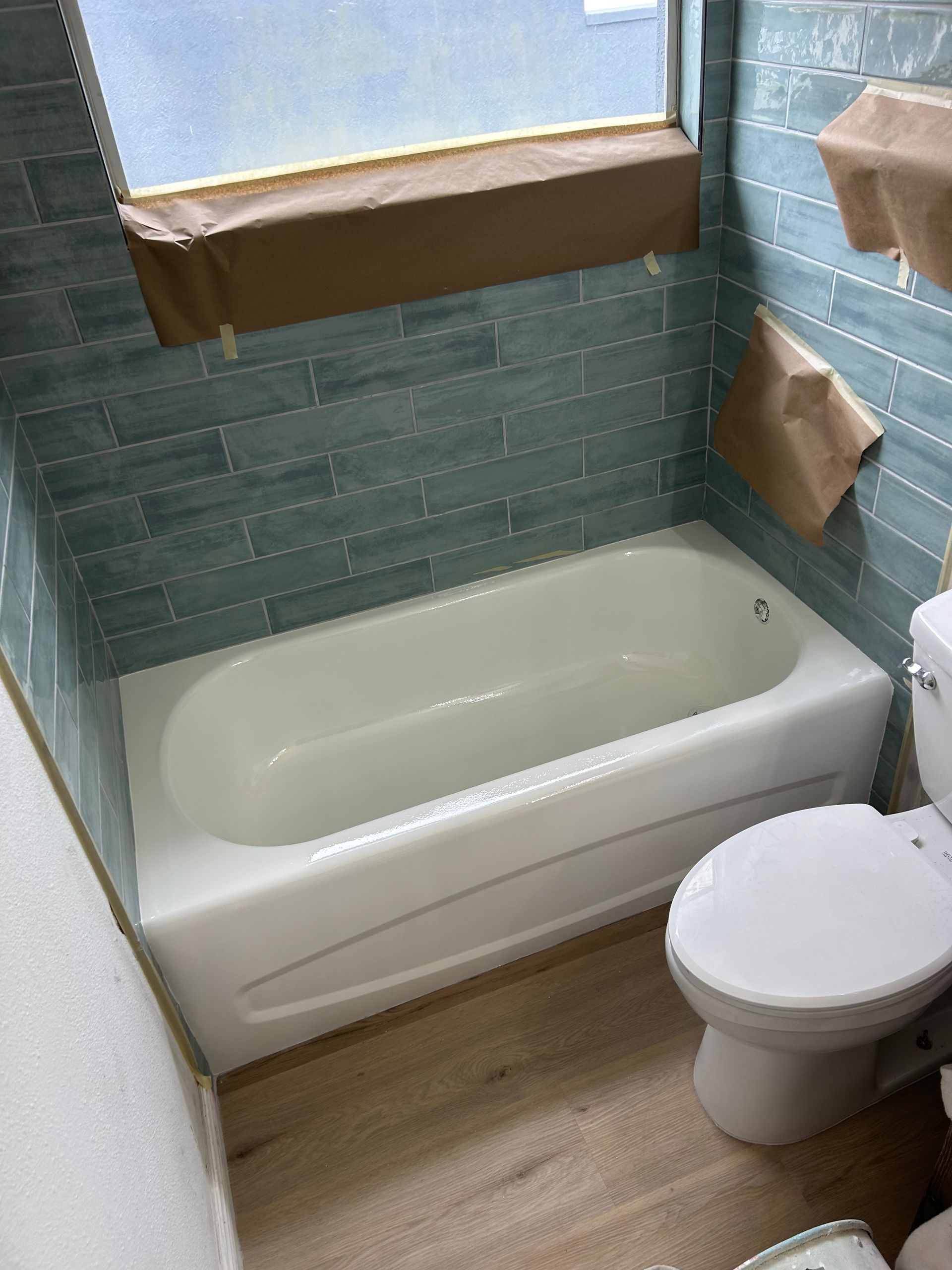 Bathroom with a white bathtub, blue tiled walls, and a toilet.