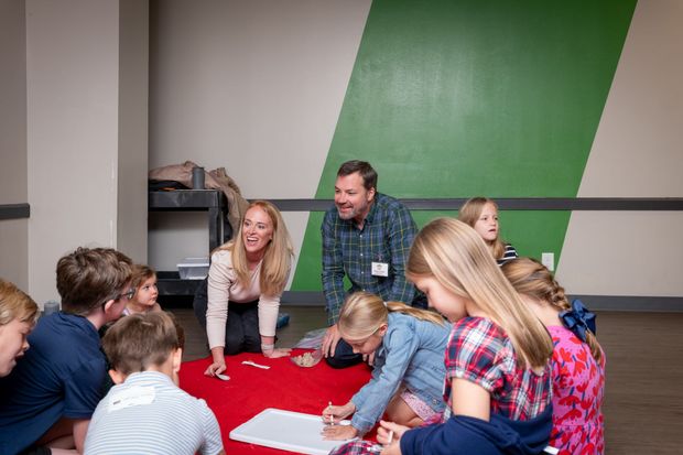 People gathered around a red tablecloth, writing and talking in a classroom or workshop setting