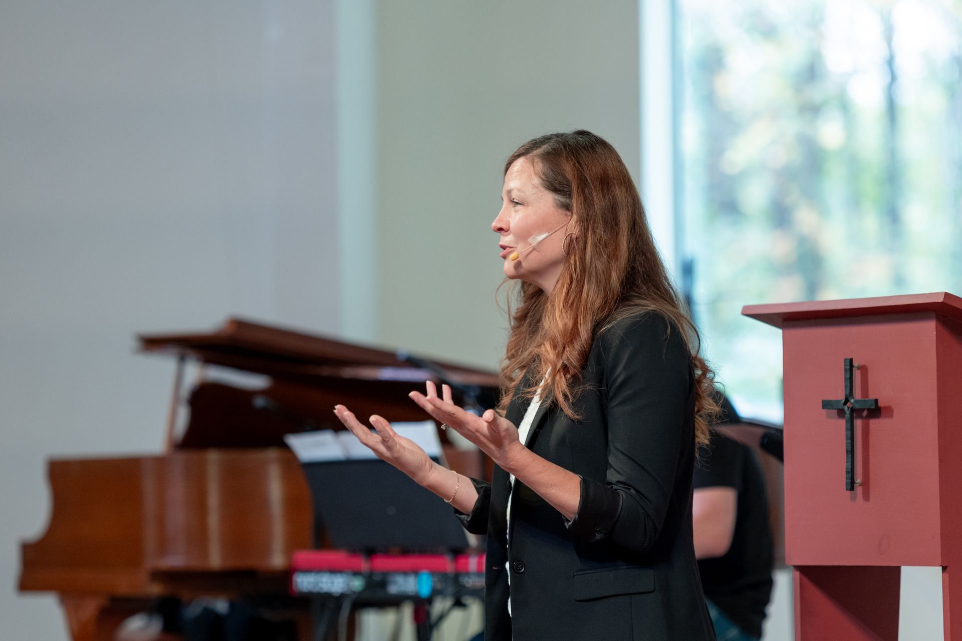 Lydnsey speaking at a podium inside Kairos church, with a grand piano in the background