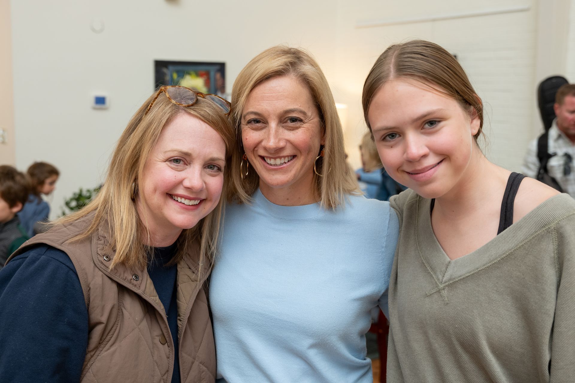 Three people smiling indoors, standing close together at an event.