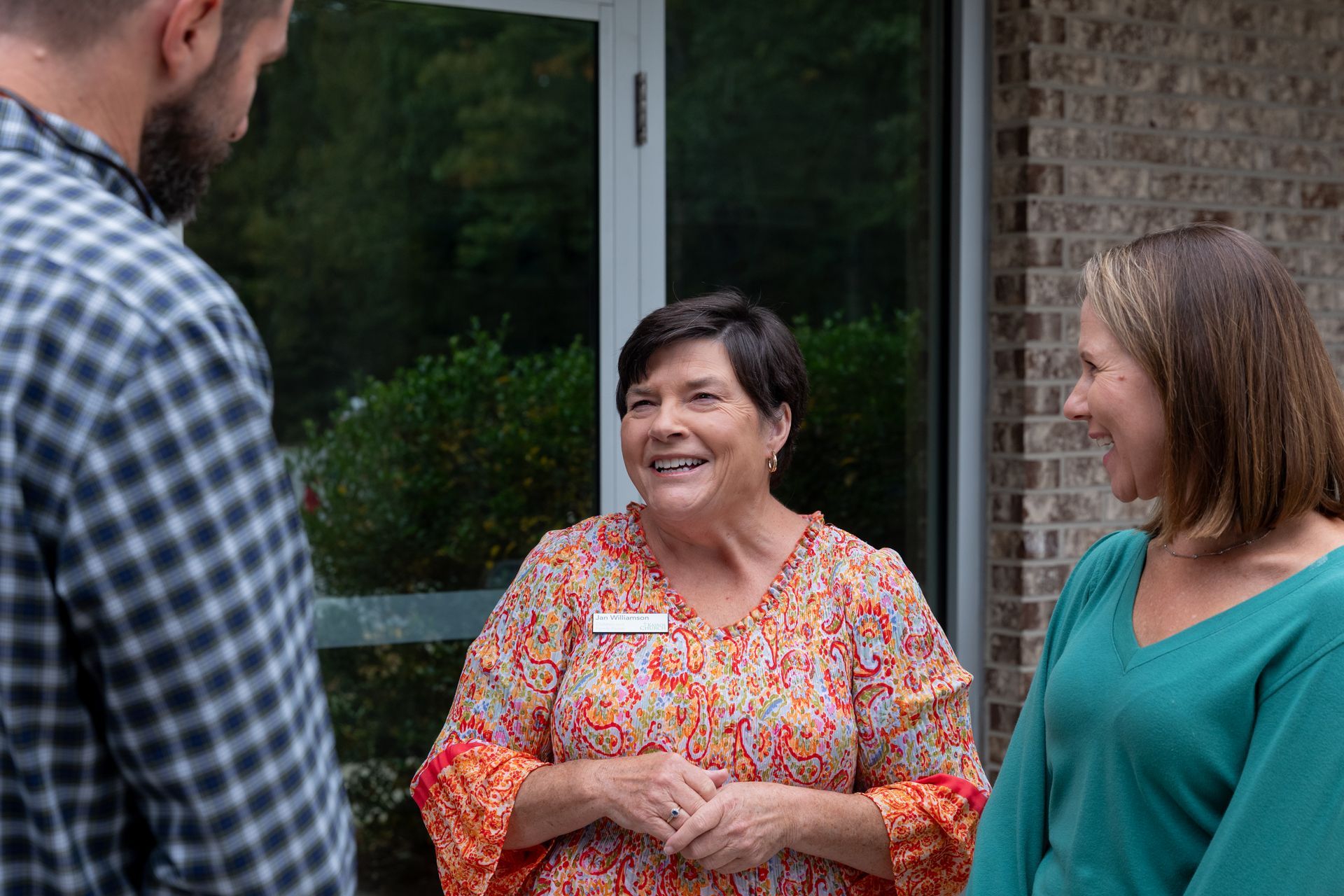 Three people chatting outside a building, smiling near a glass door.