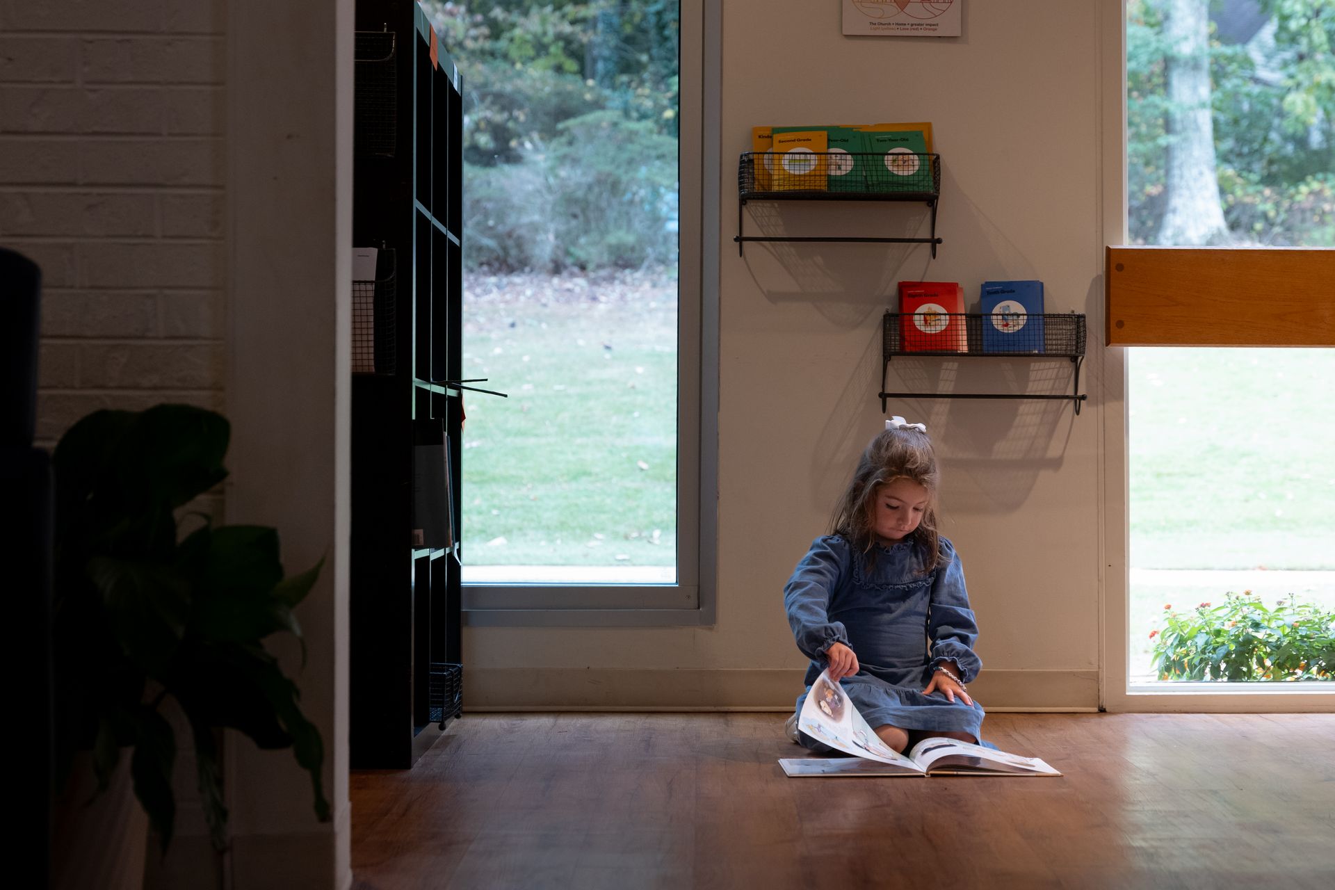 Child reading a book on the floor by a window in a bright room