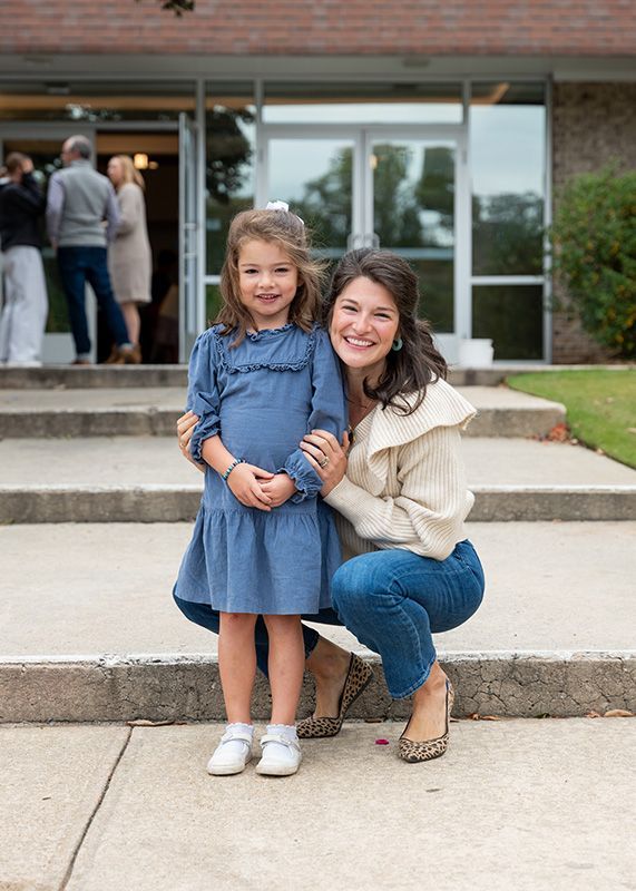 Woman crouches beside smiling child on steps outside a building