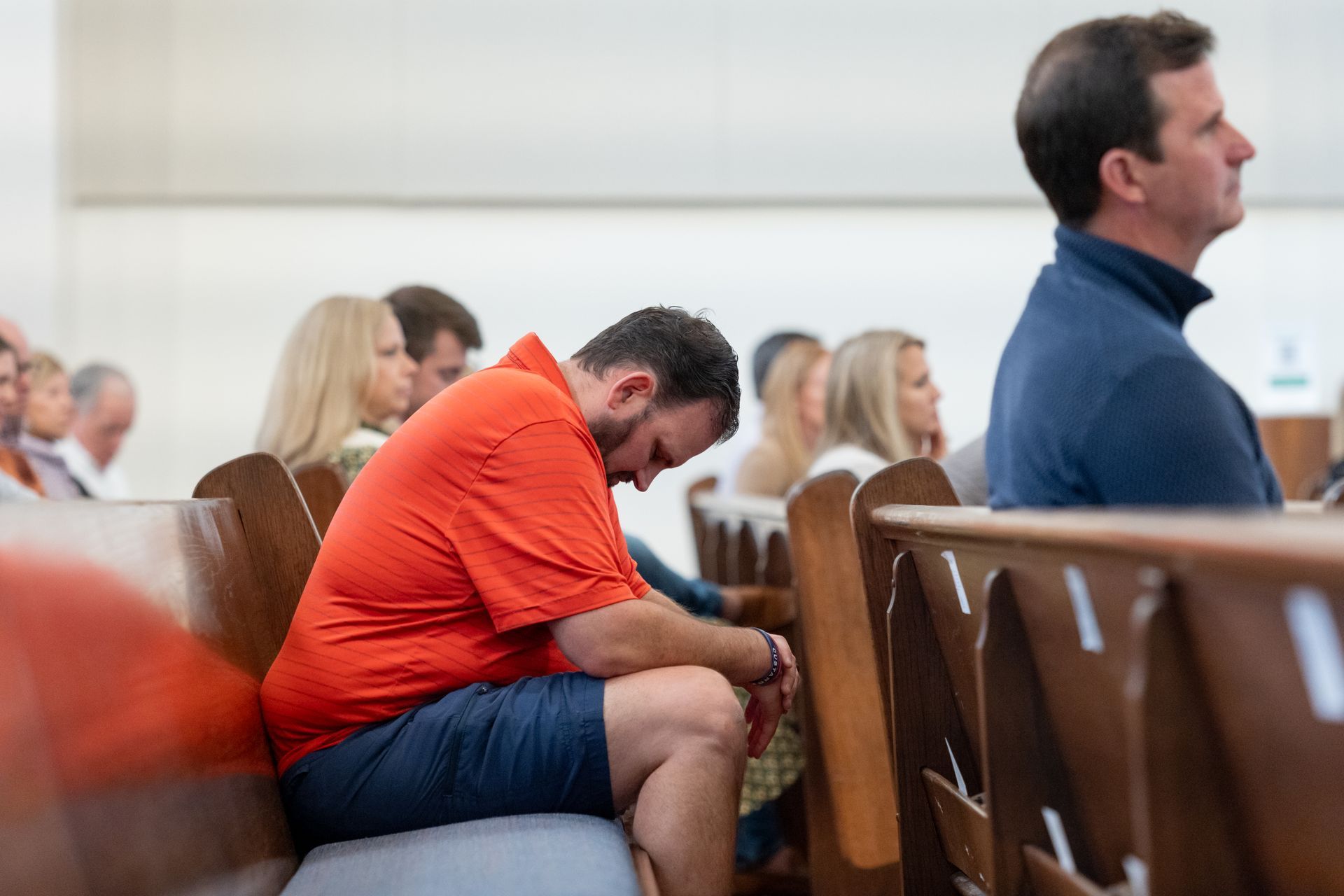 Man in orange shirt sits hunched forward on a chair during worship
