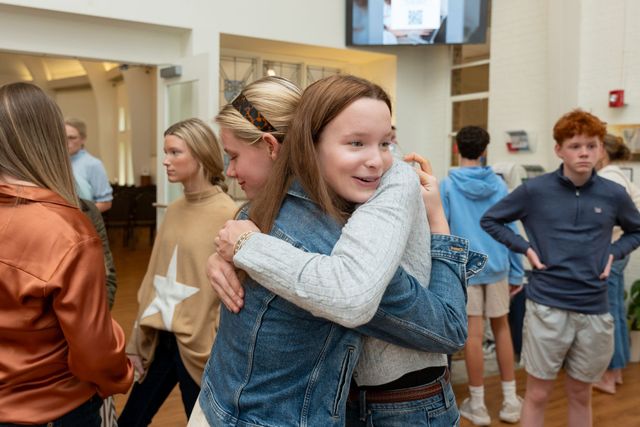 Children hugging in a bright indoor room with others standing nearby