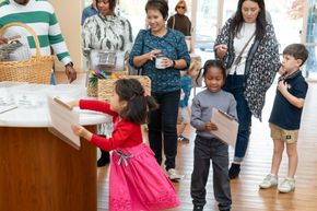Children in a classroom line up to place papers into a box during an activity