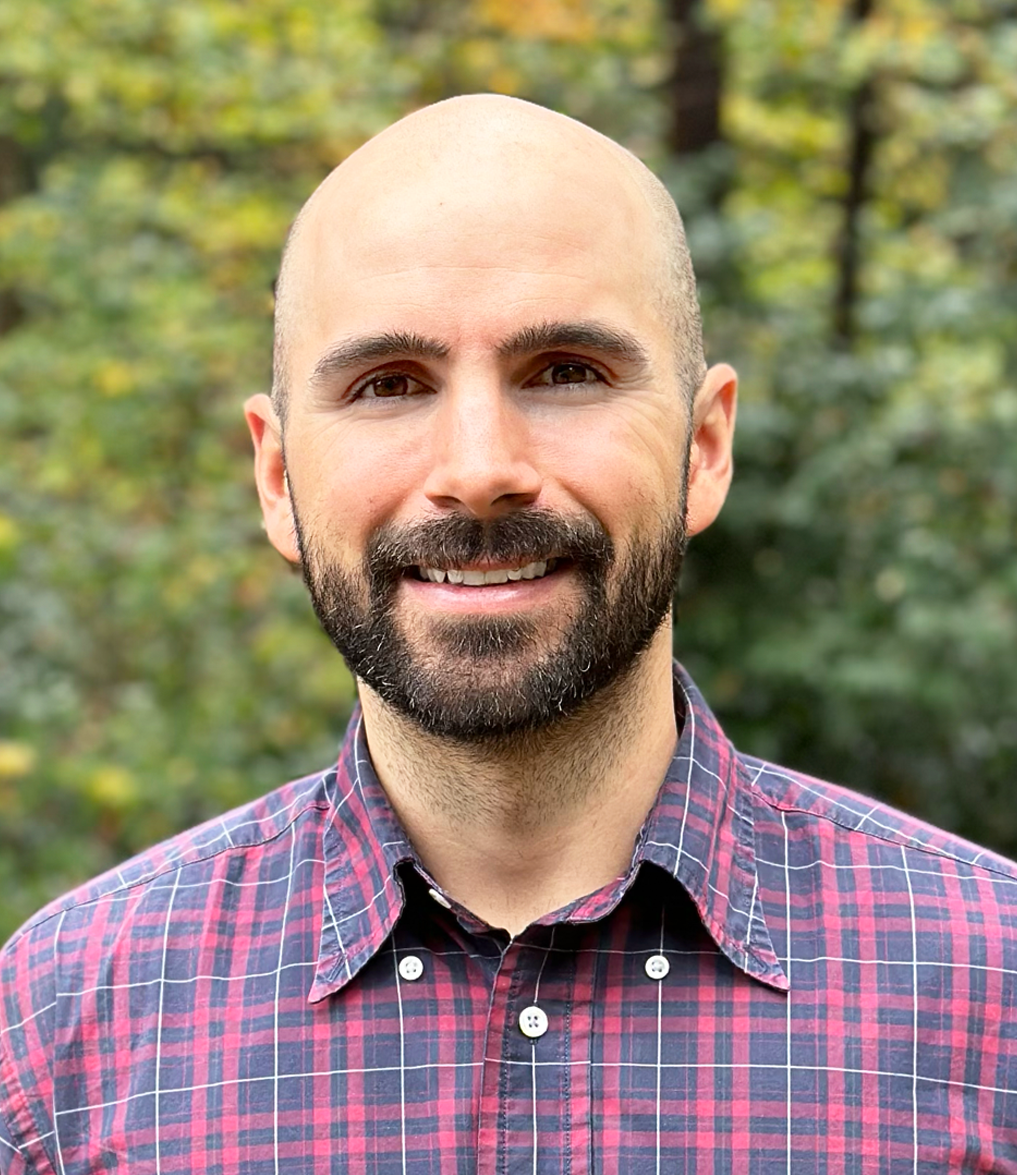 Marchant smiling wearing a red plaid shirt outdoors with blurred greenery