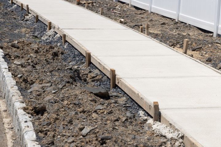 Newly poured concrete sidewalk with wooden forms and surrounding dirt.