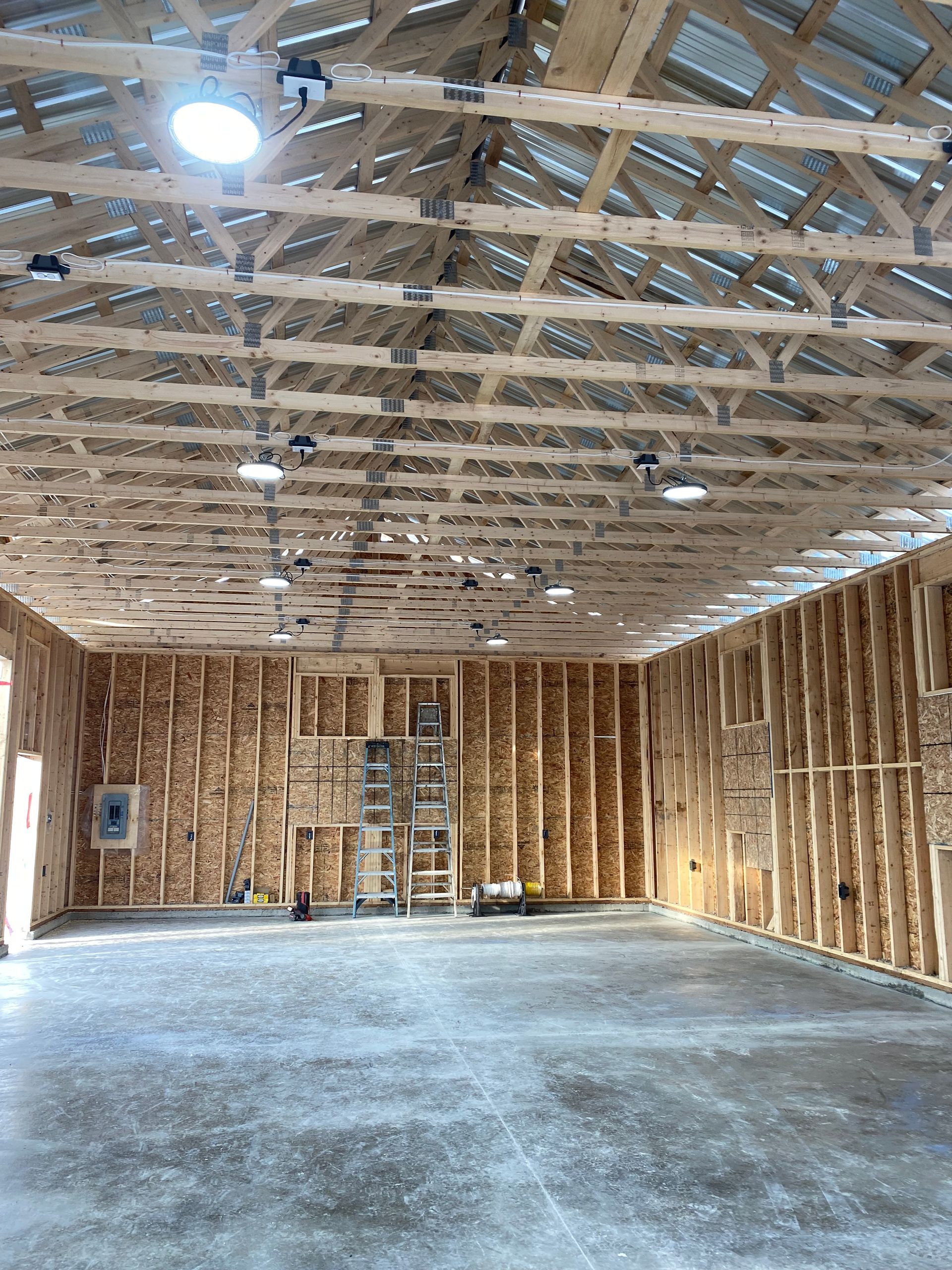 Interior of a large unfinished building with wooden framework, concrete floor, and overhead lighting.