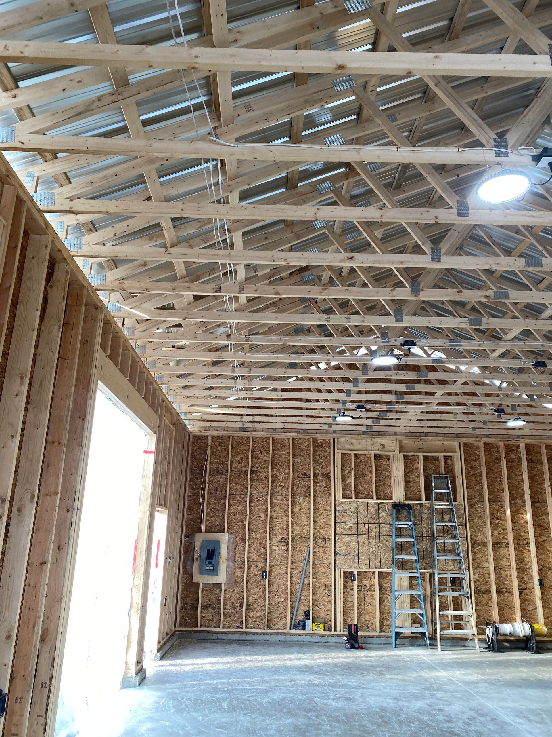 Unfinished wooden interior of a building. Framing, trusses, and metal roofing are visible.