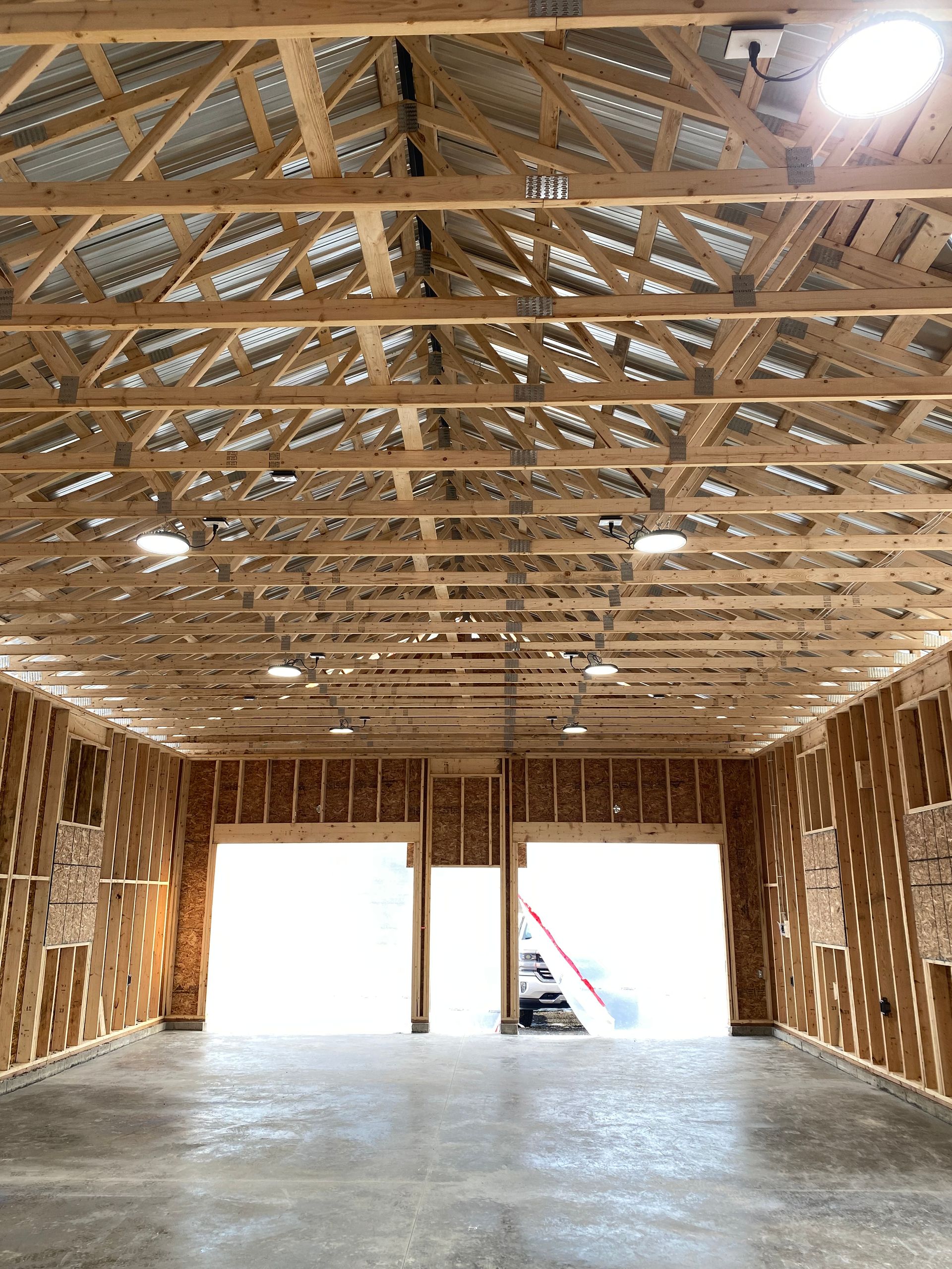 Interior view of a wooden framed structure with open garage door frames and overhead lighting.