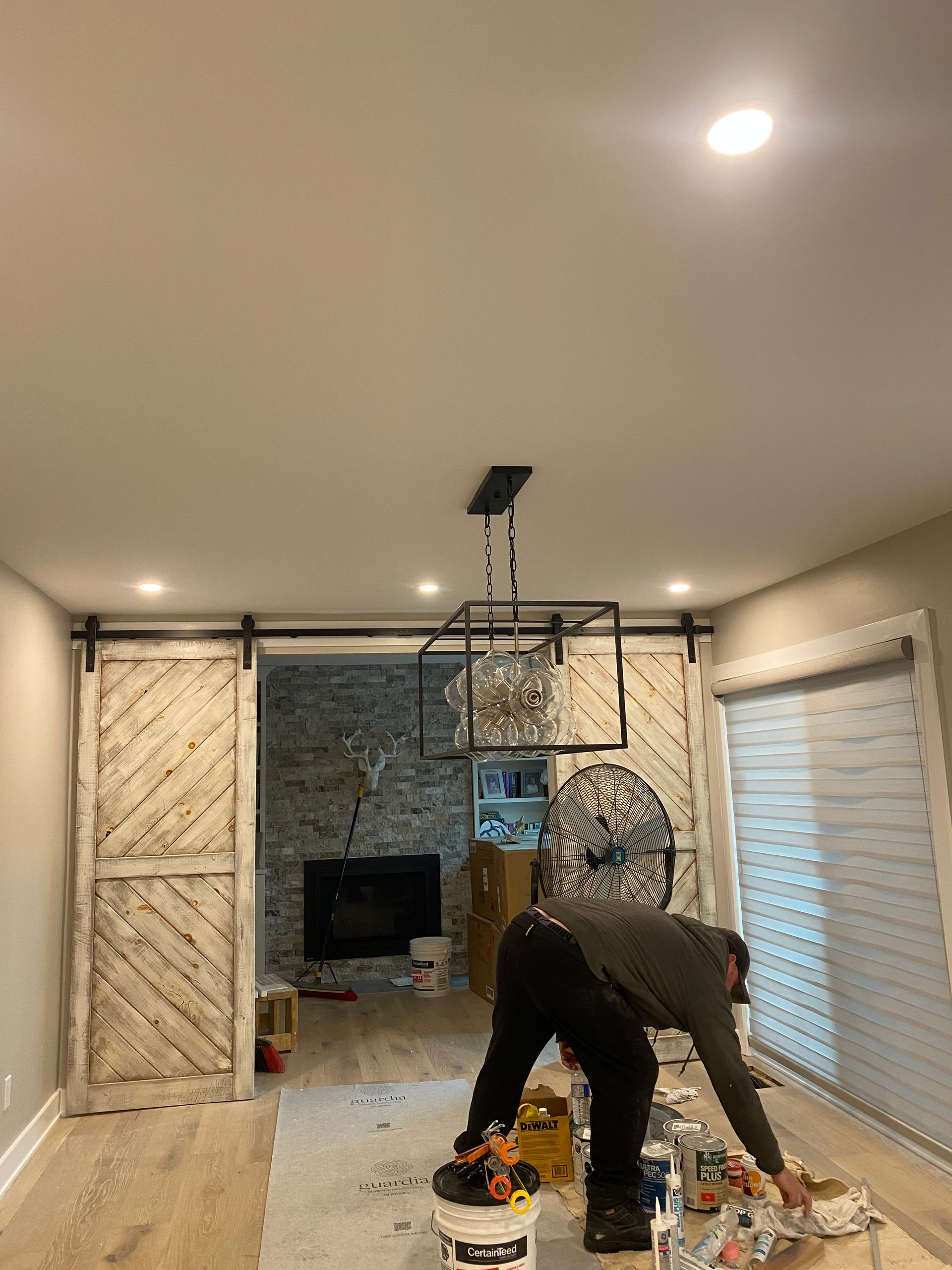 Man painting in a room with light wood floors, a fireplace, and barn doors. A chandelier hangs from the ceiling.