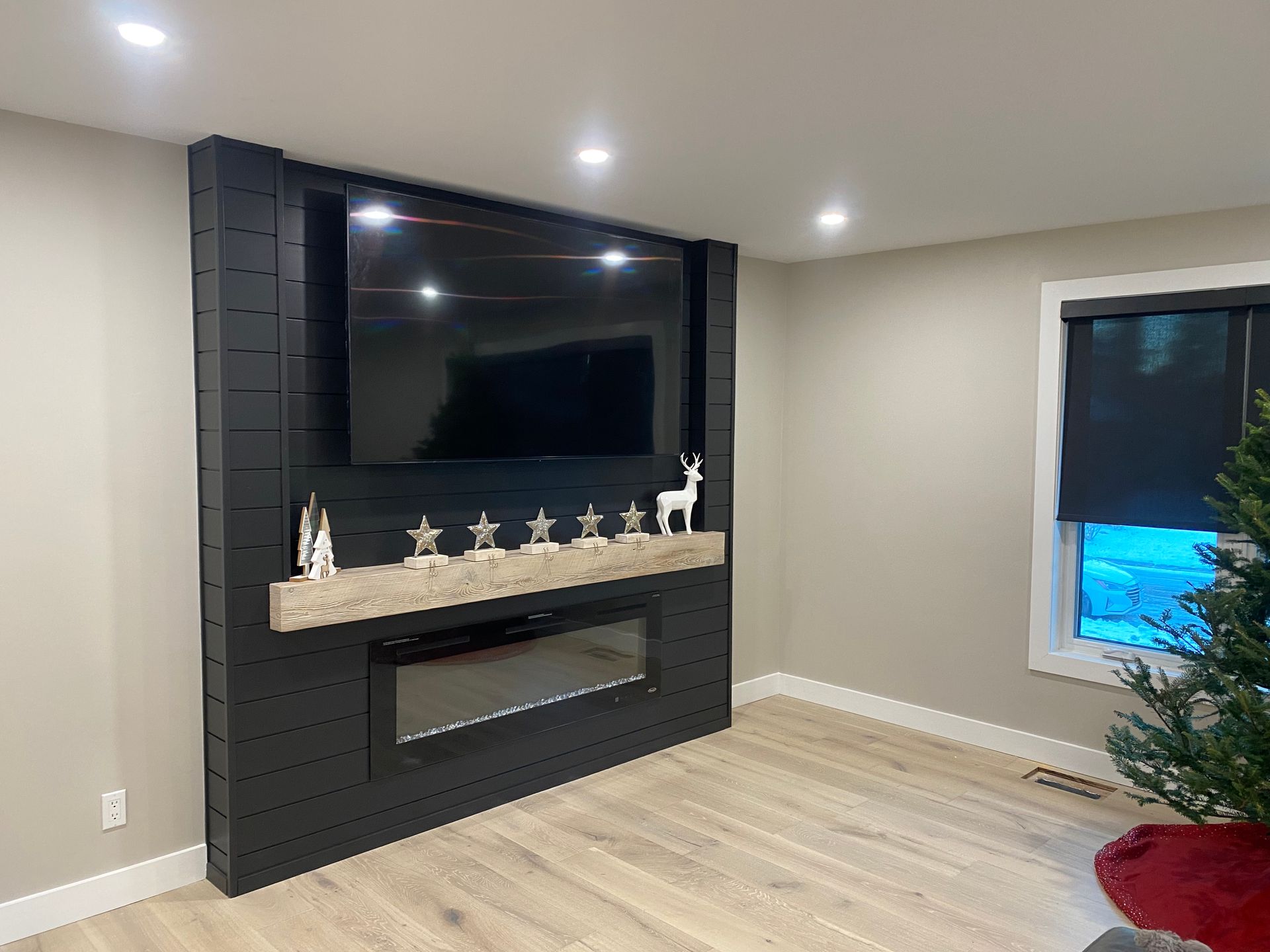 Black fireplace and TV wall with decorations in a living room; a window is to the right.