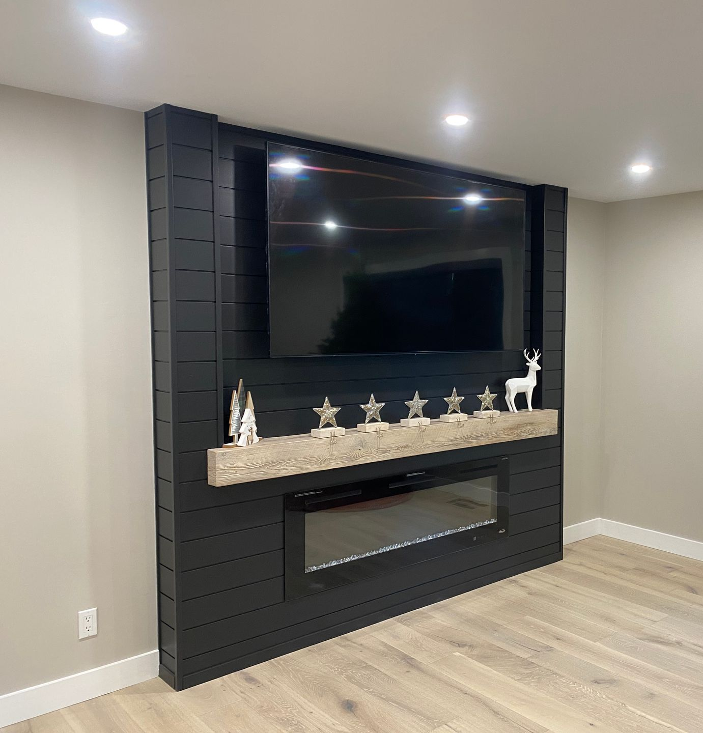 Black shiplap accent wall with TV, fireplace, and decorative shelf.  Beige walls, light wood floor.