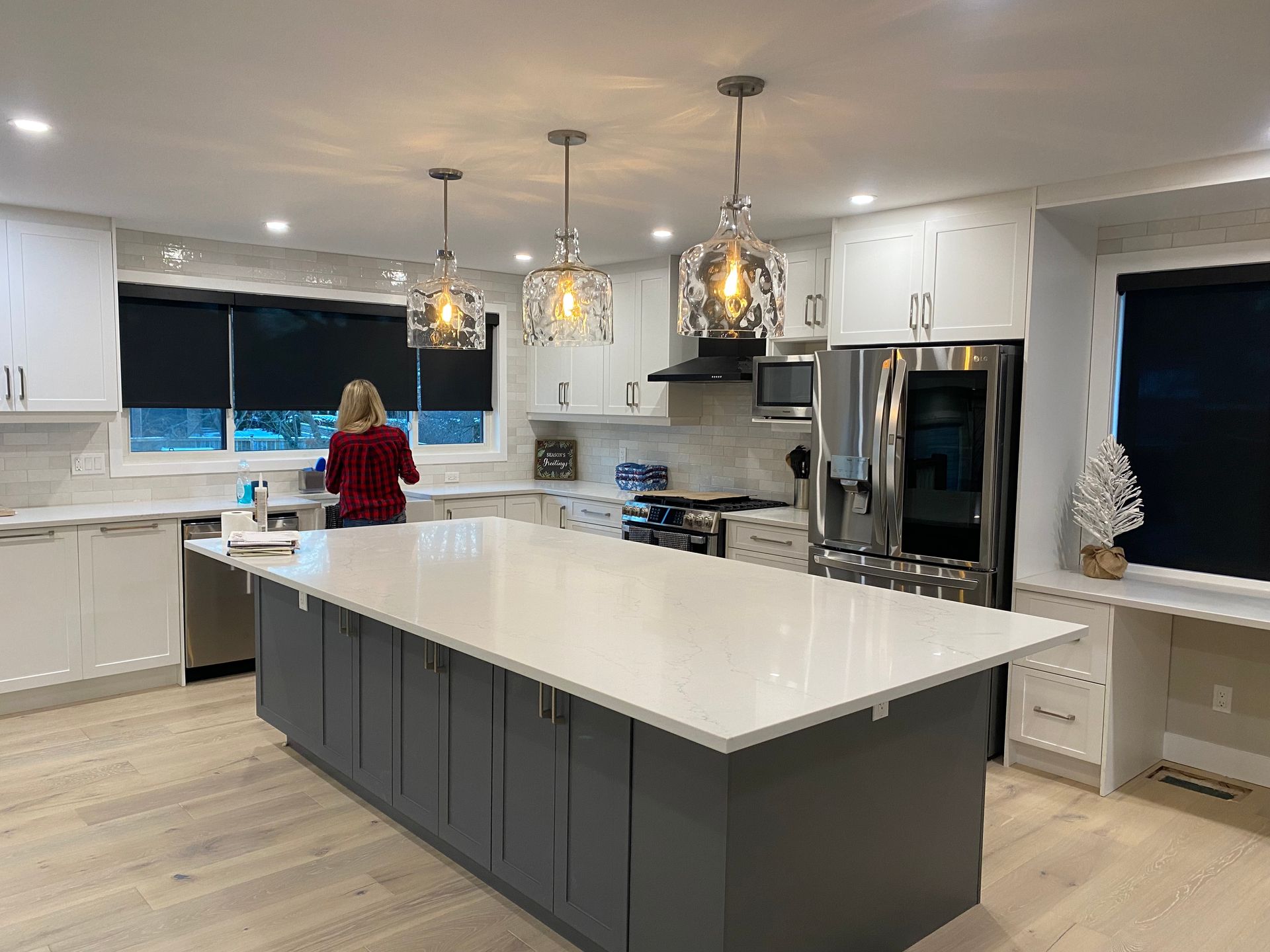 Modern kitchen with large gray island, white cabinets, and woman at the counter.