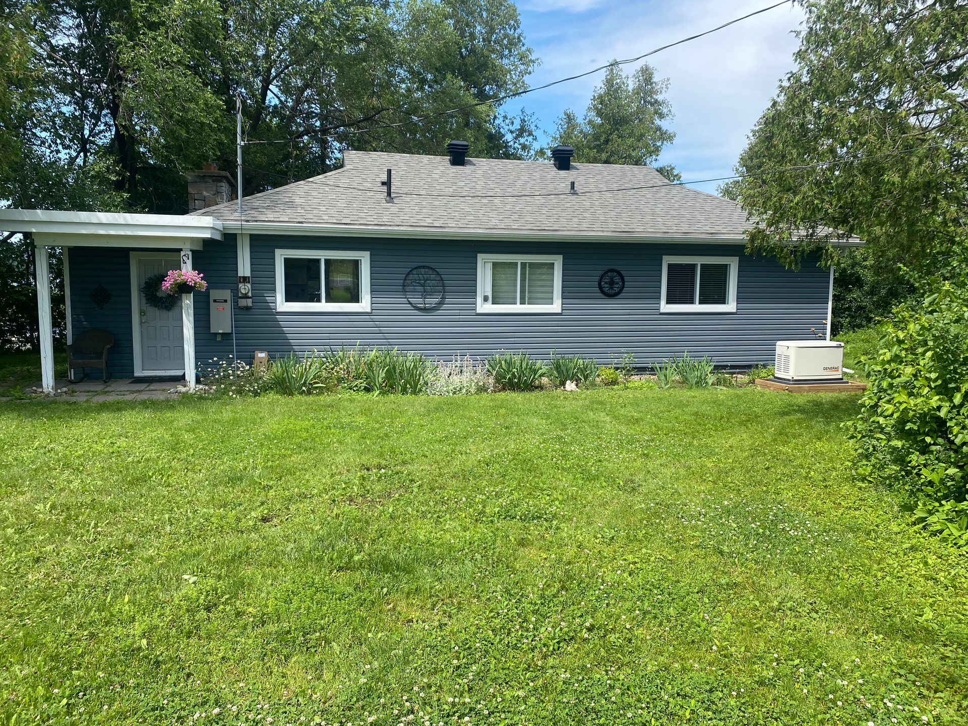 Blue-sided bungalow with white-trimmed windows and a small front yard filled with green grass.