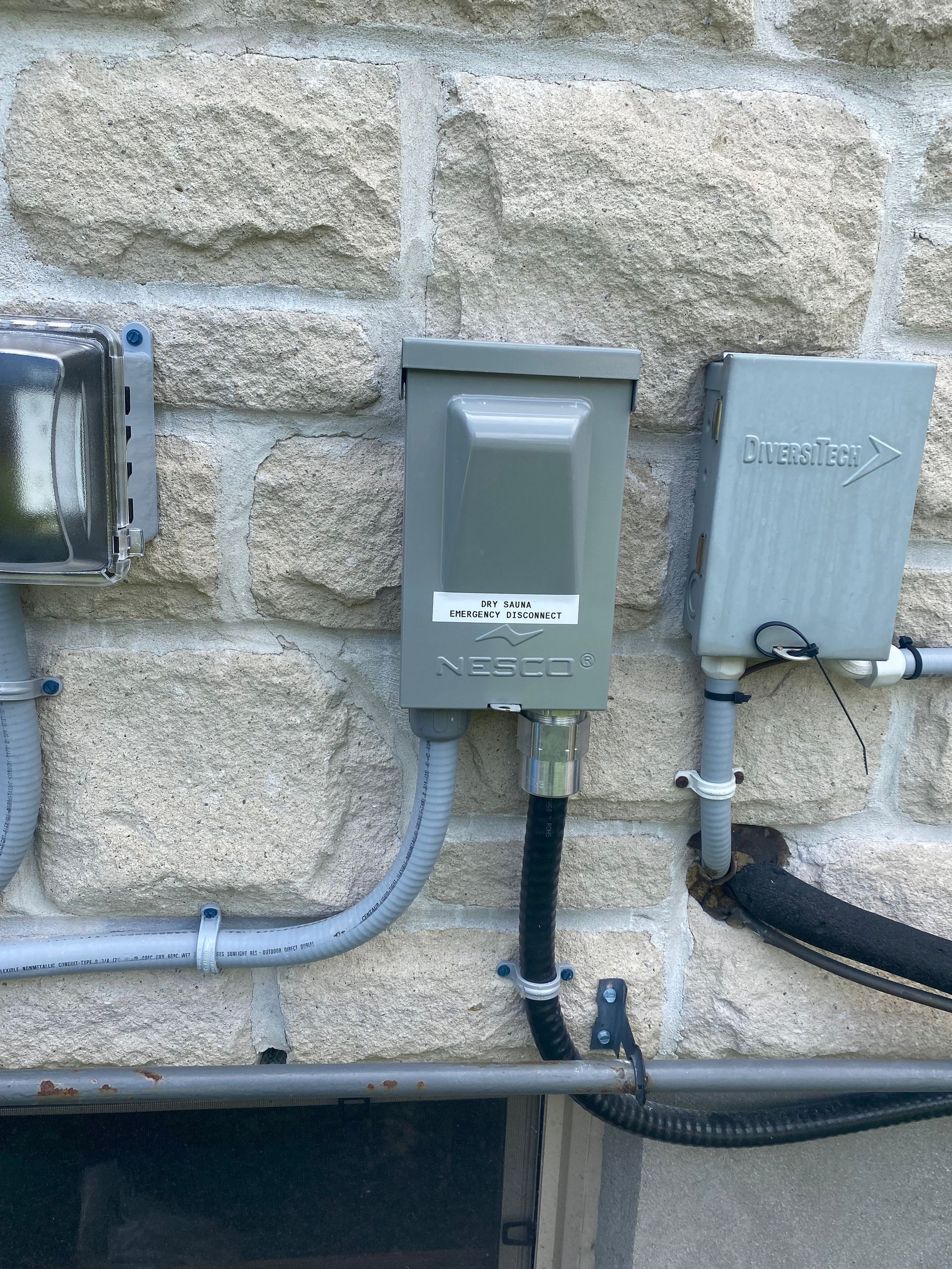 Electrical boxes on a stone wall: a gray service disconnect, a meter box, and a smaller box.