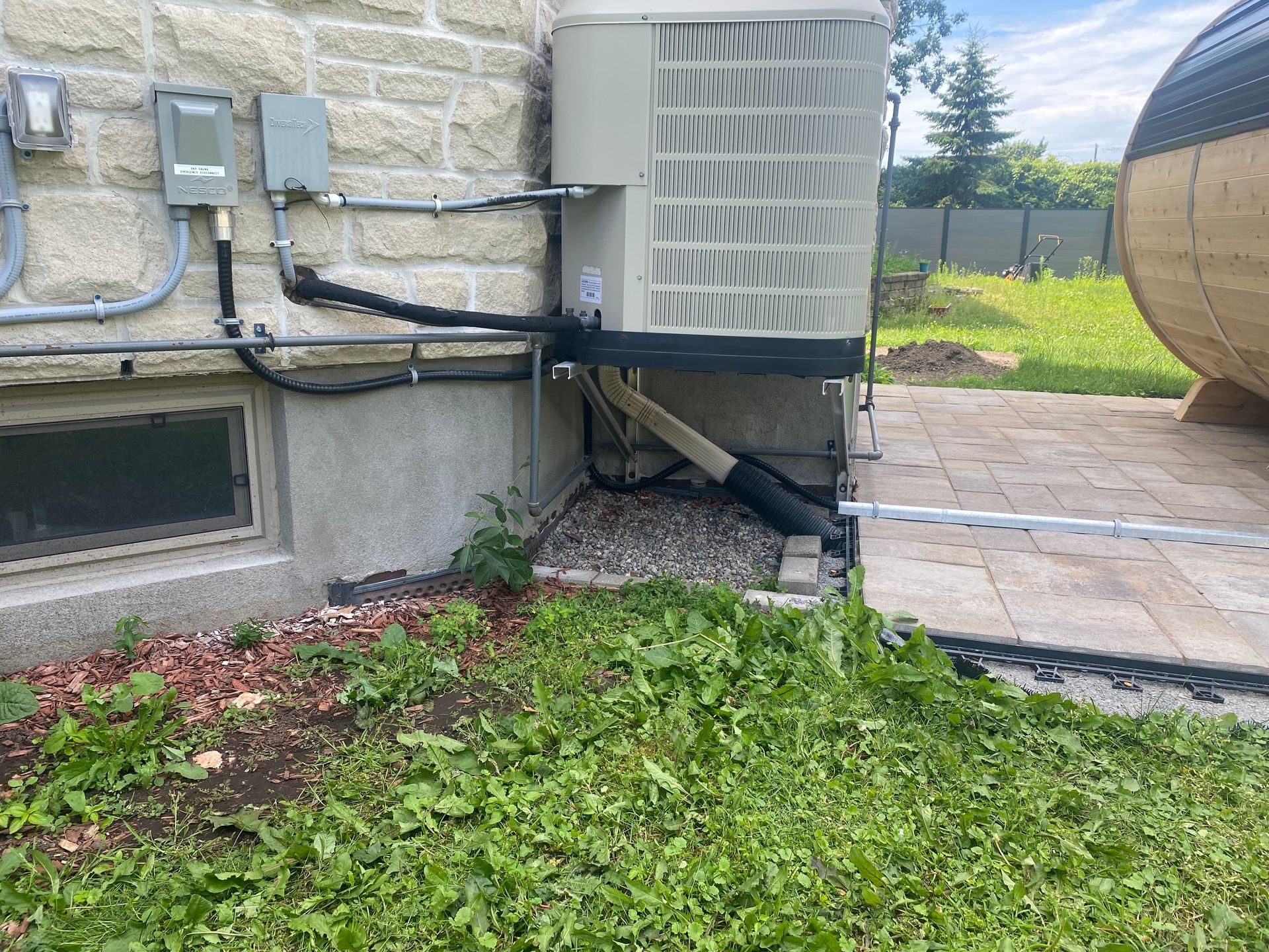 An air conditioning unit next to a stone building, near a grassy area and patio stones.