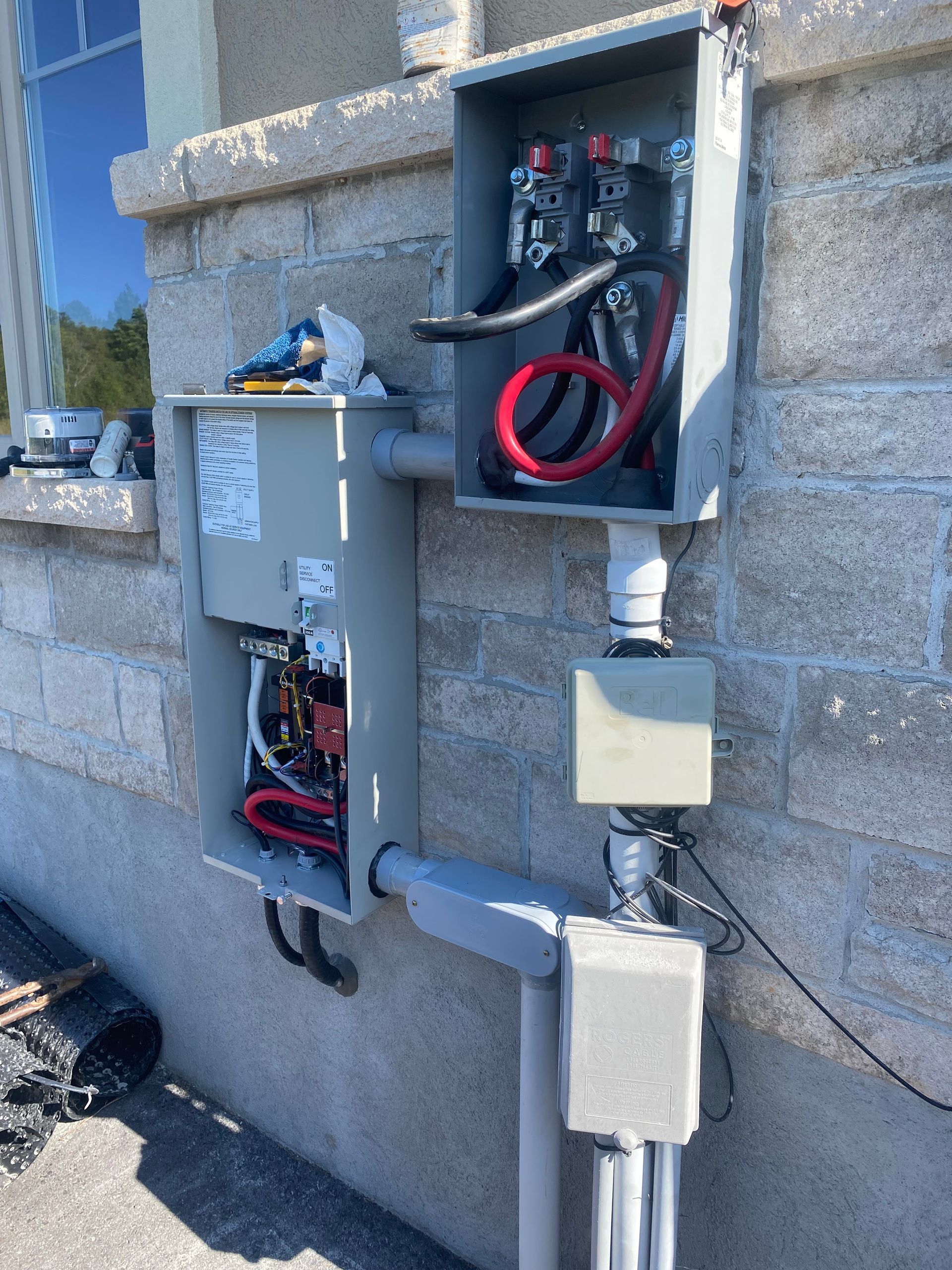 Electrical junction boxes mounted on a light-colored brick building. Exposed wiring visible. Conduit pipes connect boxes.