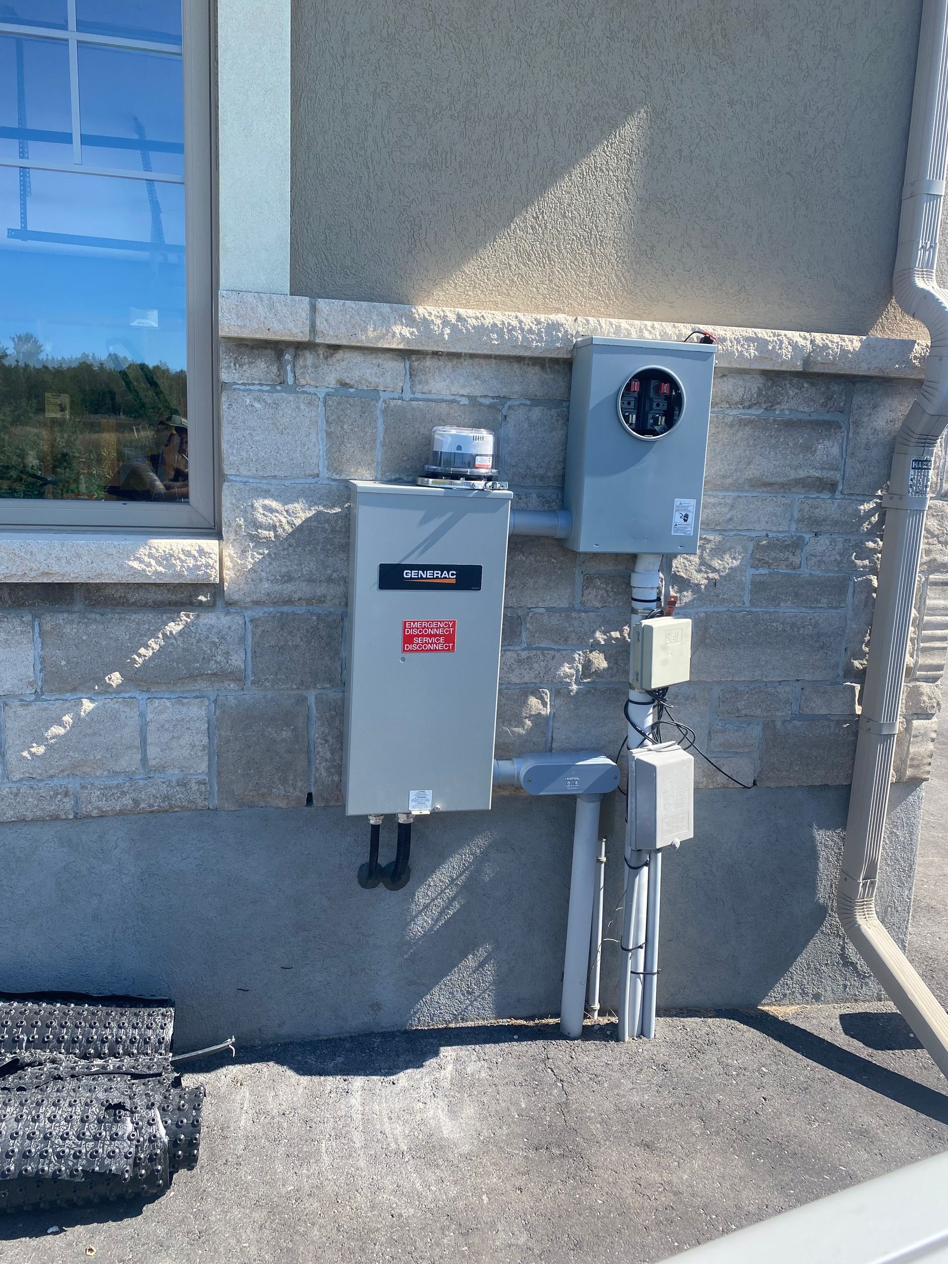 Exterior electrical panel on a light-colored brick building, featuring a meter, junction boxes, and conduits.