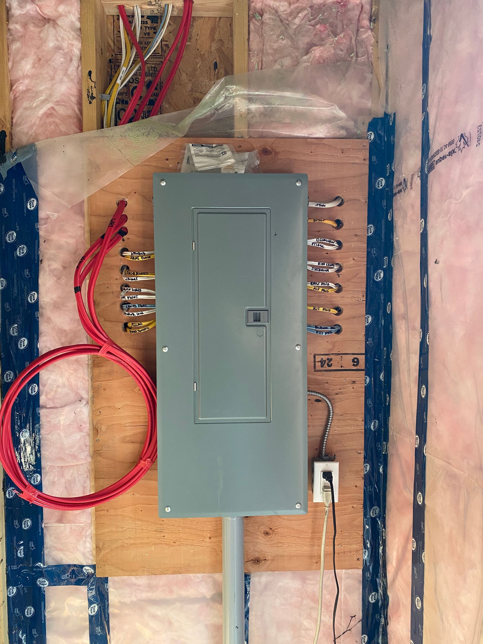 Electrical panel installation with exposed wiring on a wooden backing, surrounded by insulation.