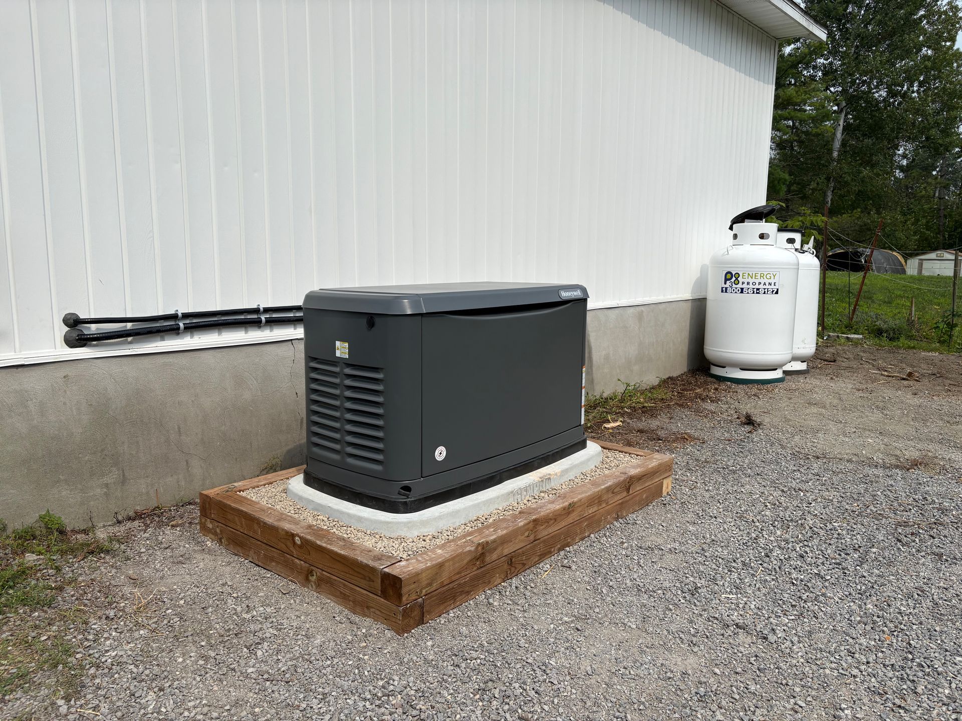 Generator outside a building next to propane tanks. Gray generator on a wooden platform.