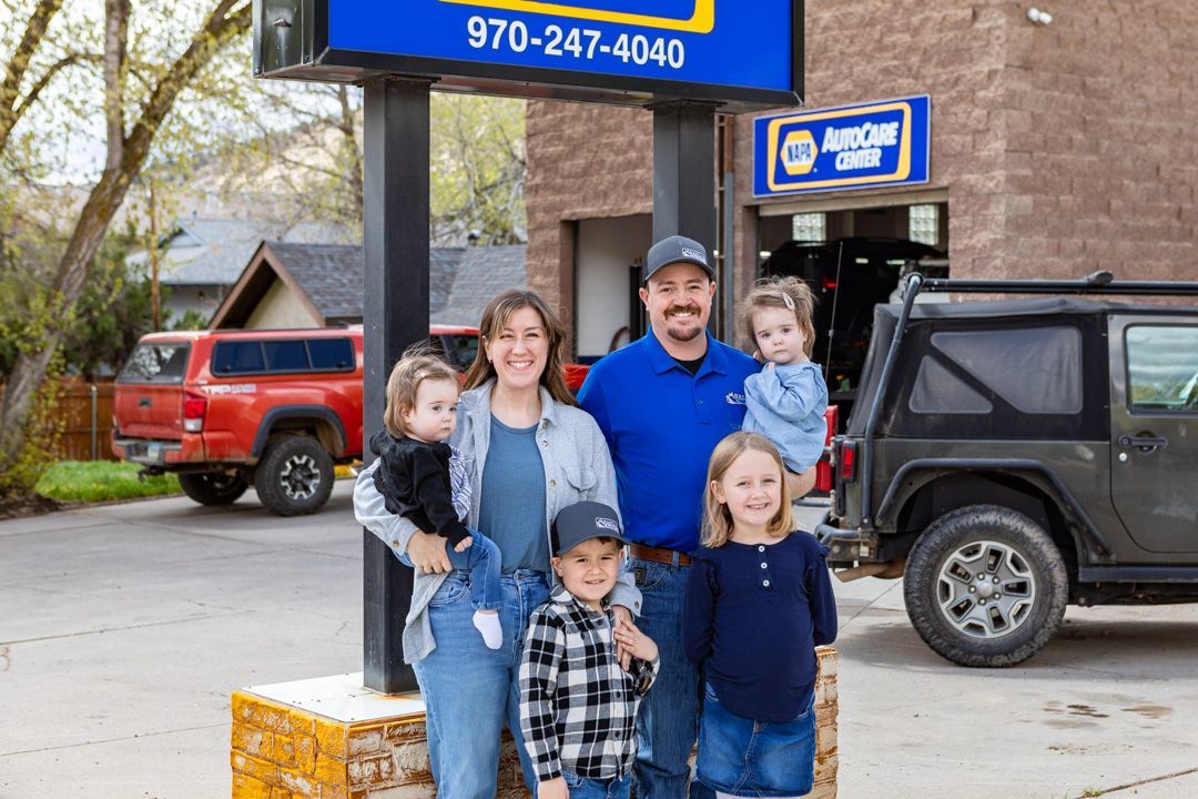 Family standing outside a storefront with a black jeep and red truck parked nearby