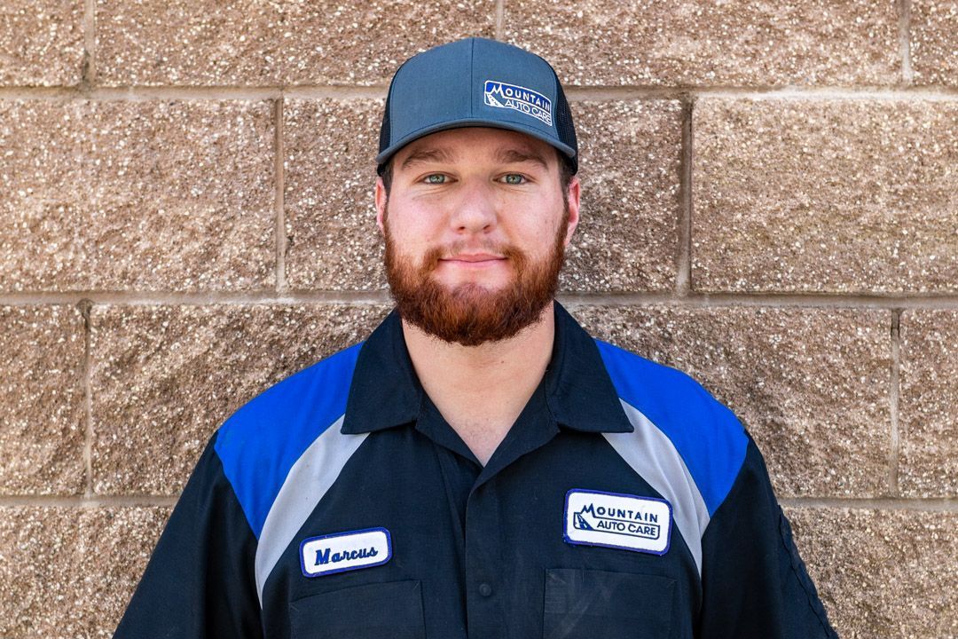 Man in blue work shirt and cap standing against a tan brick wall