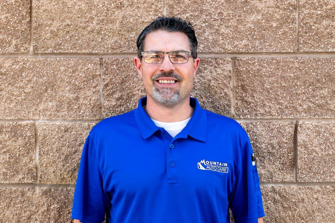Man in blue polo shirt standing against a tan brick wall, smiling at the camera