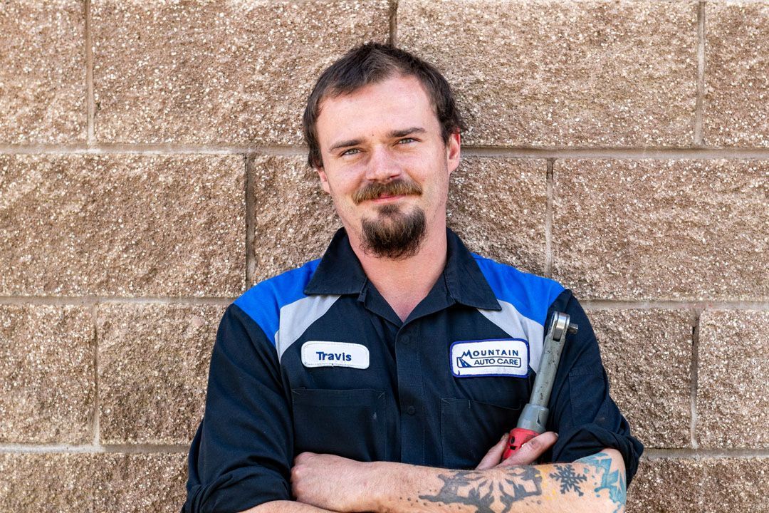 Man in navy work shirt with blue shoulder panels stands arms crossed against a tan brick wall.