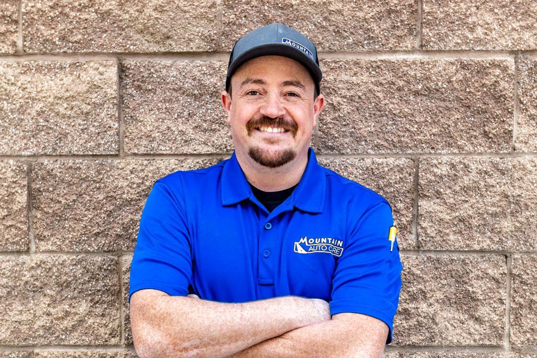 Smiling man in a blue polo and cap, standing with arms crossed against a tan brick wall.