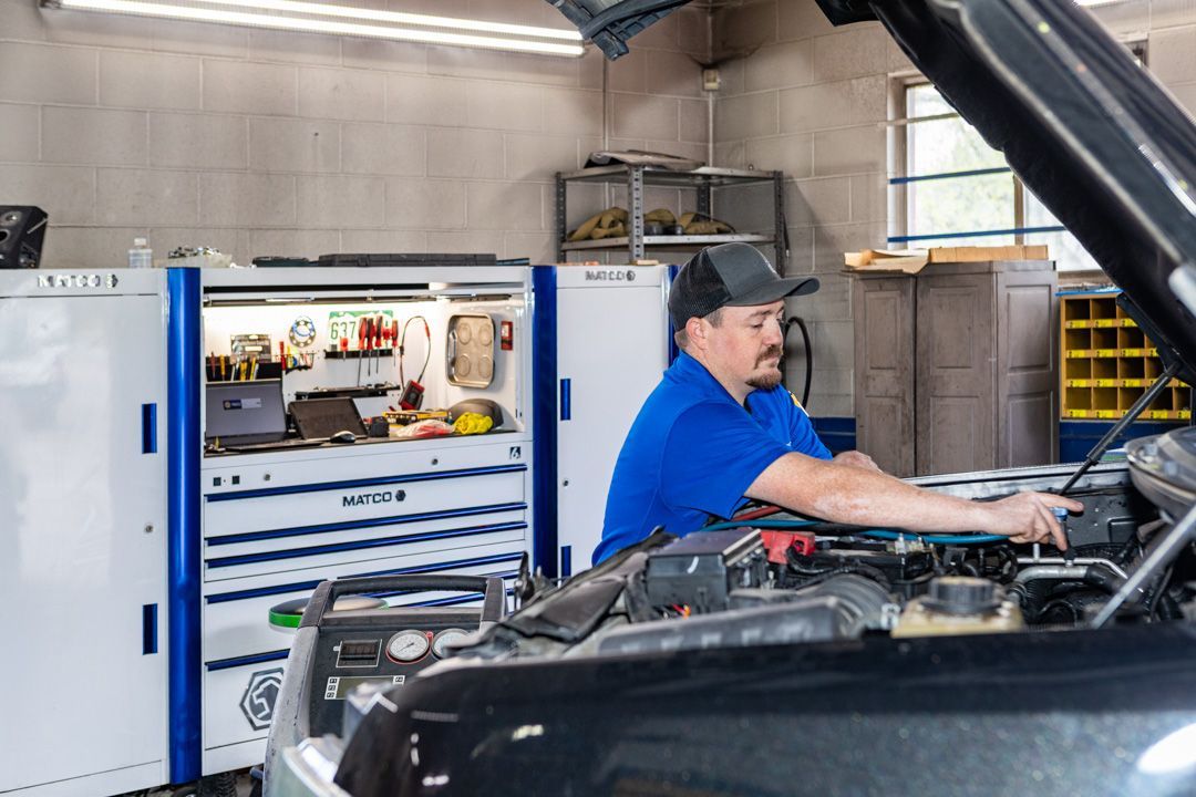 Mechanic in blue shirt working under a car hood in an auto repair garage