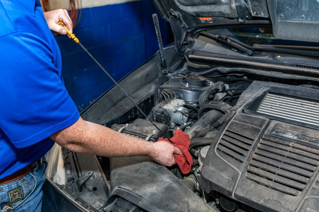 Mechanic checking engine oil under a car hood with a dipstick and red rag
