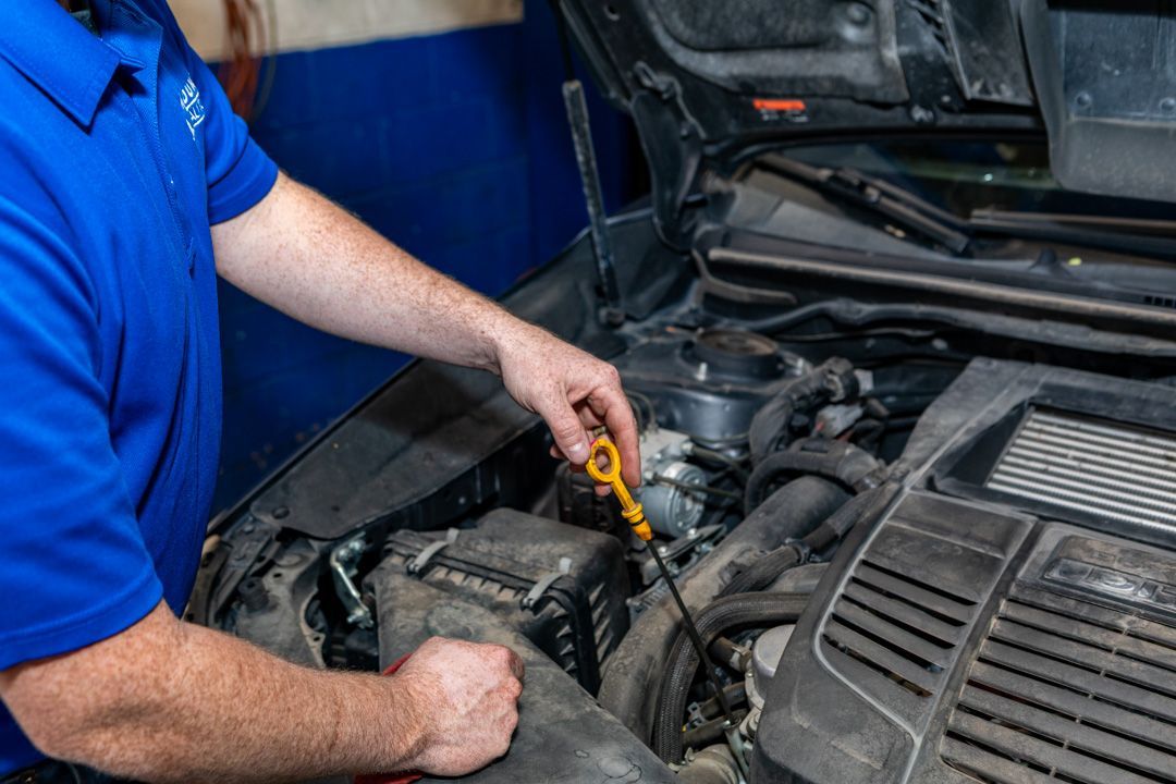 Mechanic in blue shirt checking engine oil with dipstick under an open car hood