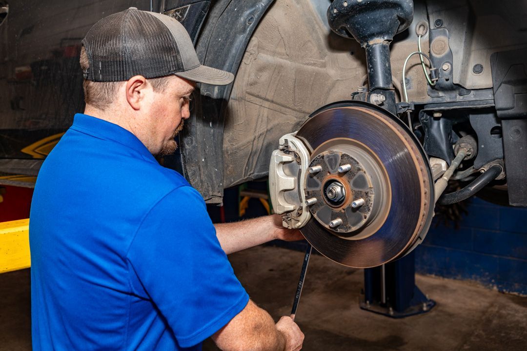 Mechanic in blue shirt inspecting a car brake rotor with tools in a garage