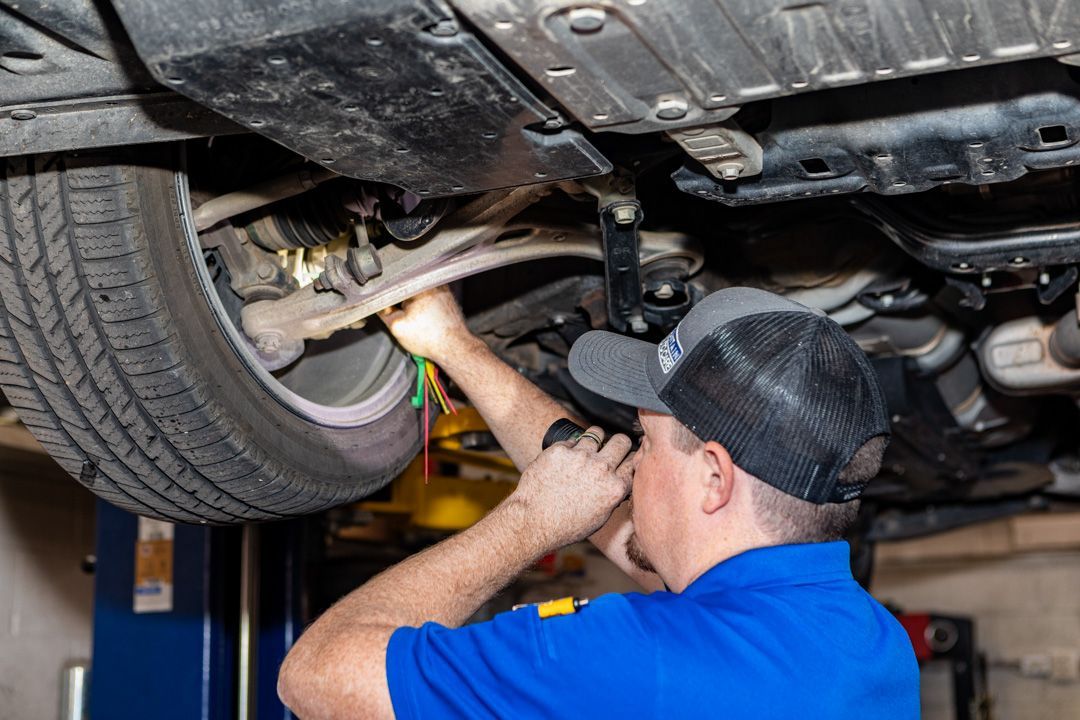 Mechanic working under a car on a lift with a wrench in an auto repair shop