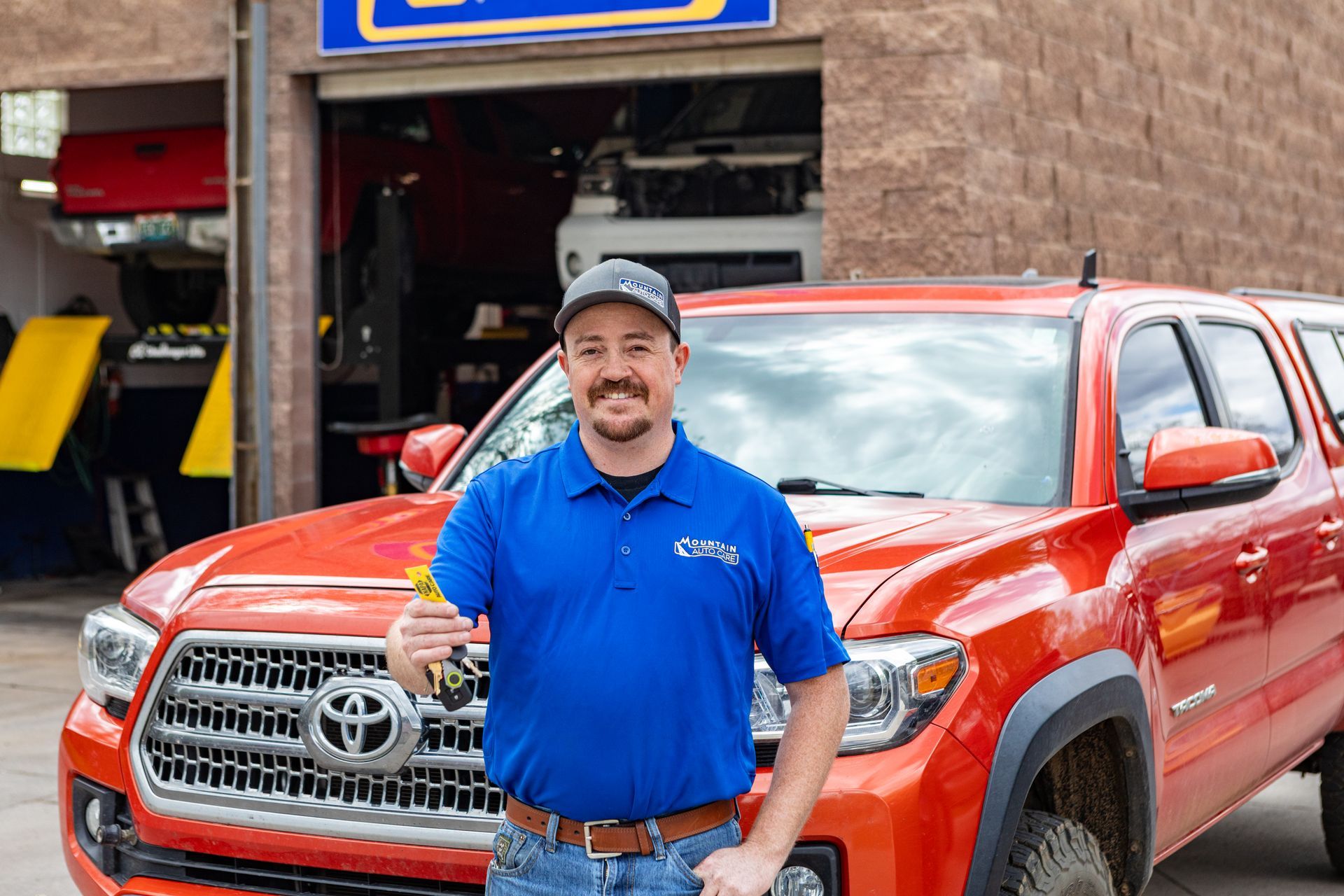 Man in blue shirt standing in front of a red Toyota truck outside a store