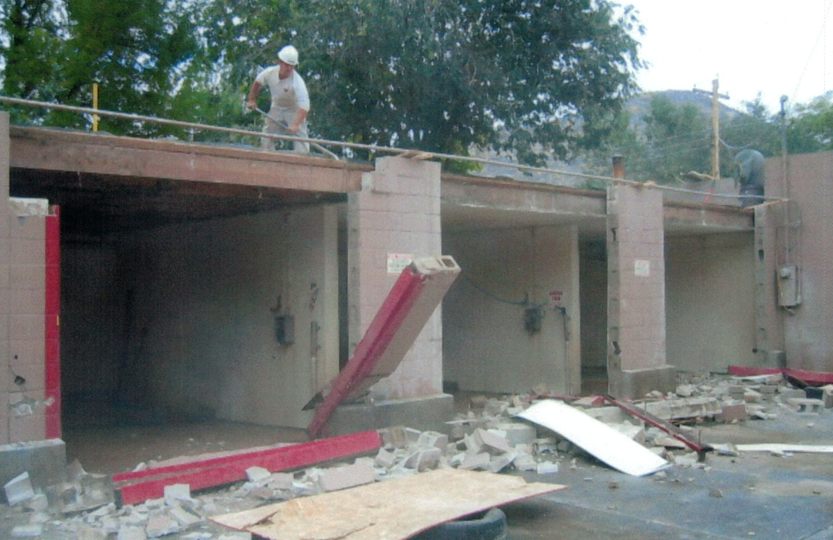 Partially collapsed building with debris, a red chute, and a worker standing on the roof