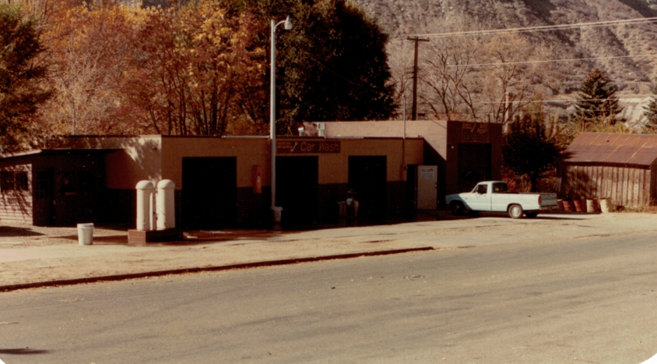 Low brick building with a white pickup truck parked outside on a quiet street, desert hillside behind.